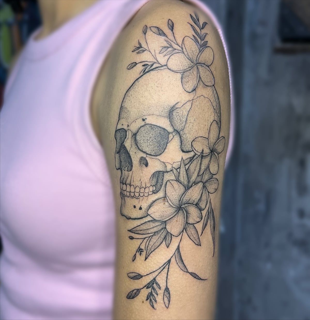 Caveira pontilhada cercada por flores de plumérias em fine line